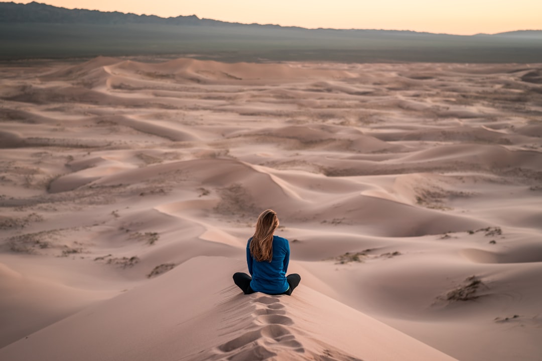 Persona sentada en una duna de arena con vistas al vasto desierto al atardecer, disfrutando de la vista para reducir el estrés.
